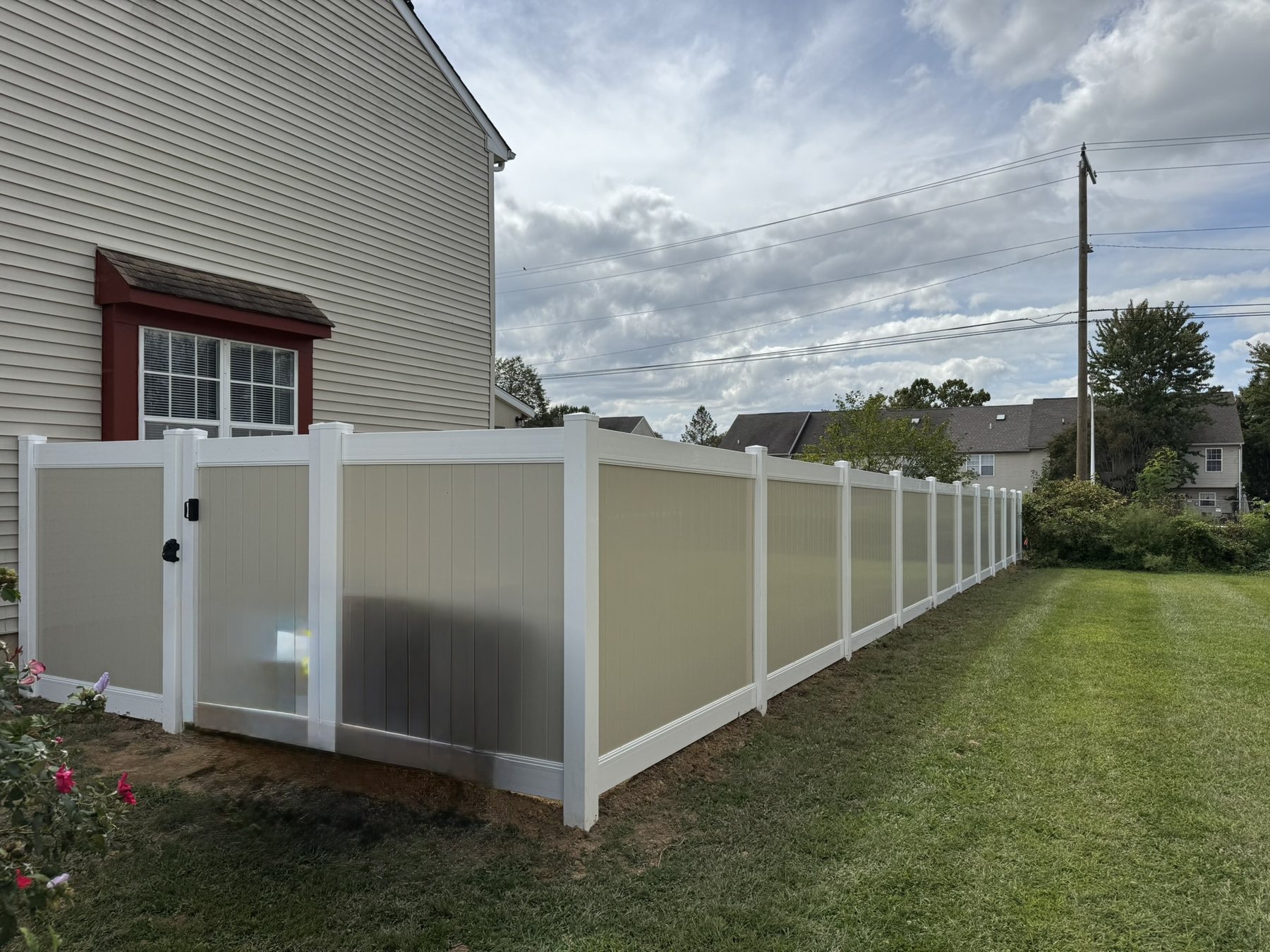 Two-tone vinyl privacy fence with khaki panels and white posts beside a home