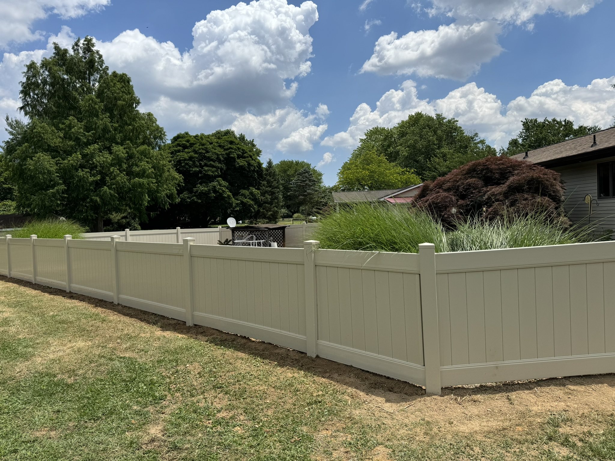 Tan vinyl privacy fence bordering a landscaped Kent County backyard